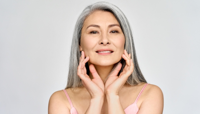 Portrait of gorgeous beautiful middle aged mature asian woman, senior older 50 year lady looking at camera touching her face isolated on white. Ads of lifting anti wrinkle skin care, spa.